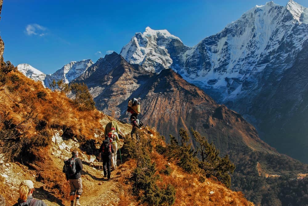 A group of people hiking up a mountain in the Great Himalayan National Park in Nepal, amidst breathtaking enhancements of nature.