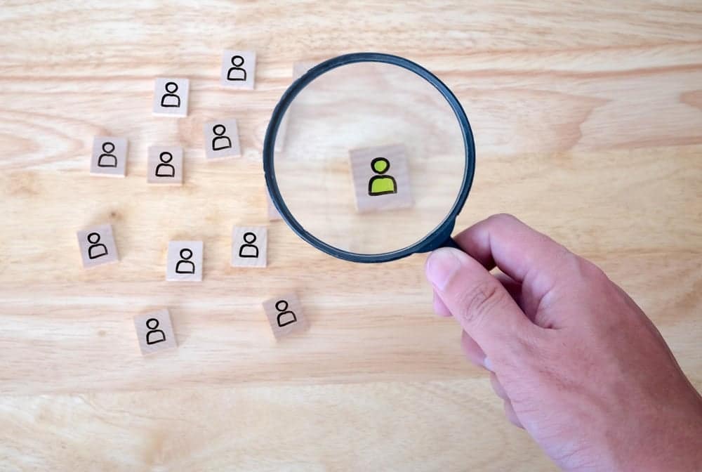 A person is holding a magnifying glass over a group of people.