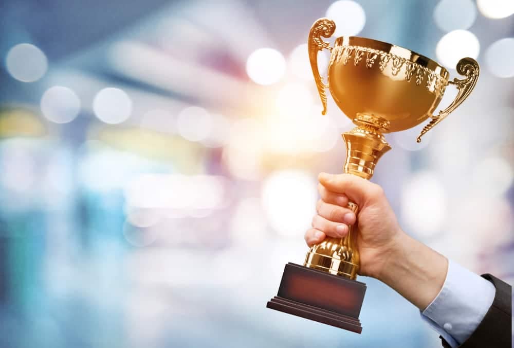 A hand holding a gold trophy in front of a blurred background, symbolizing the achievement of being a National Recipient in the Community Sport for All Initiative by the Canadian Parks & Recreation Association.