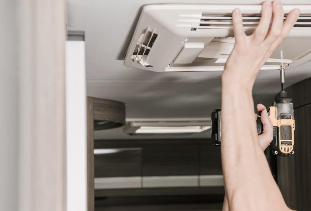 A person with RVTI training using a screwdriver to fix an air conditioner in a mobile RV.