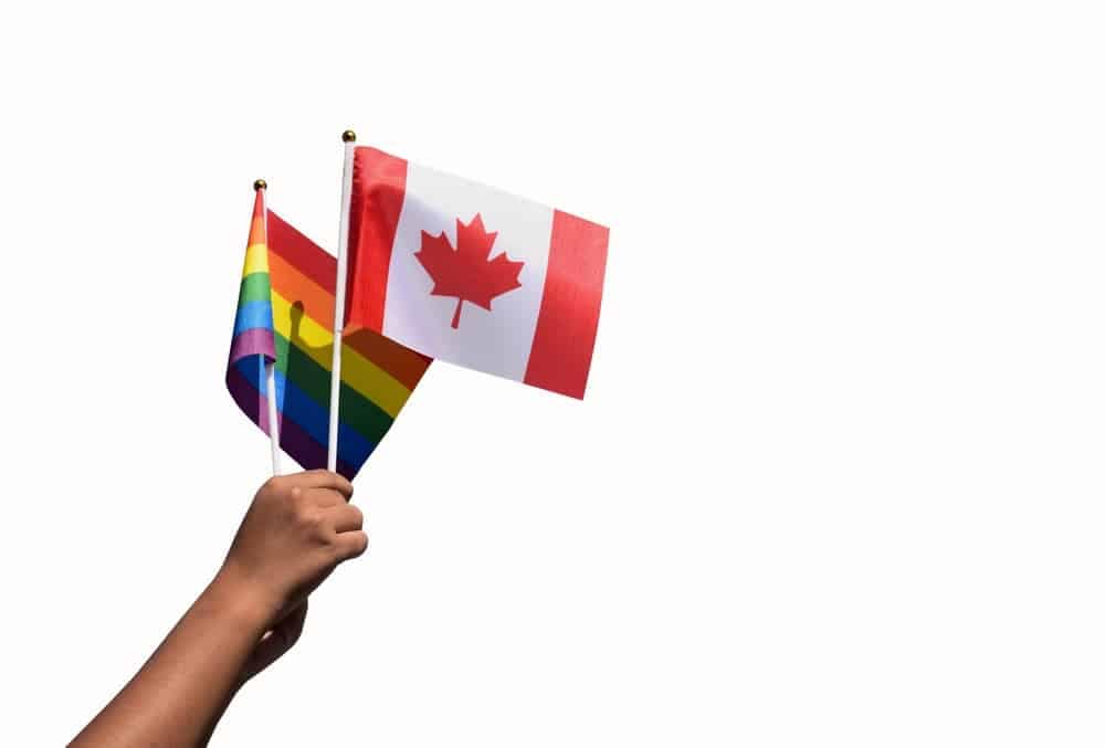 A person proudly holds two Canadian flags adorned with the iconic rainbow colors of the LGBT community, symbolizing inclusivity and support for LGBTQ travelers.