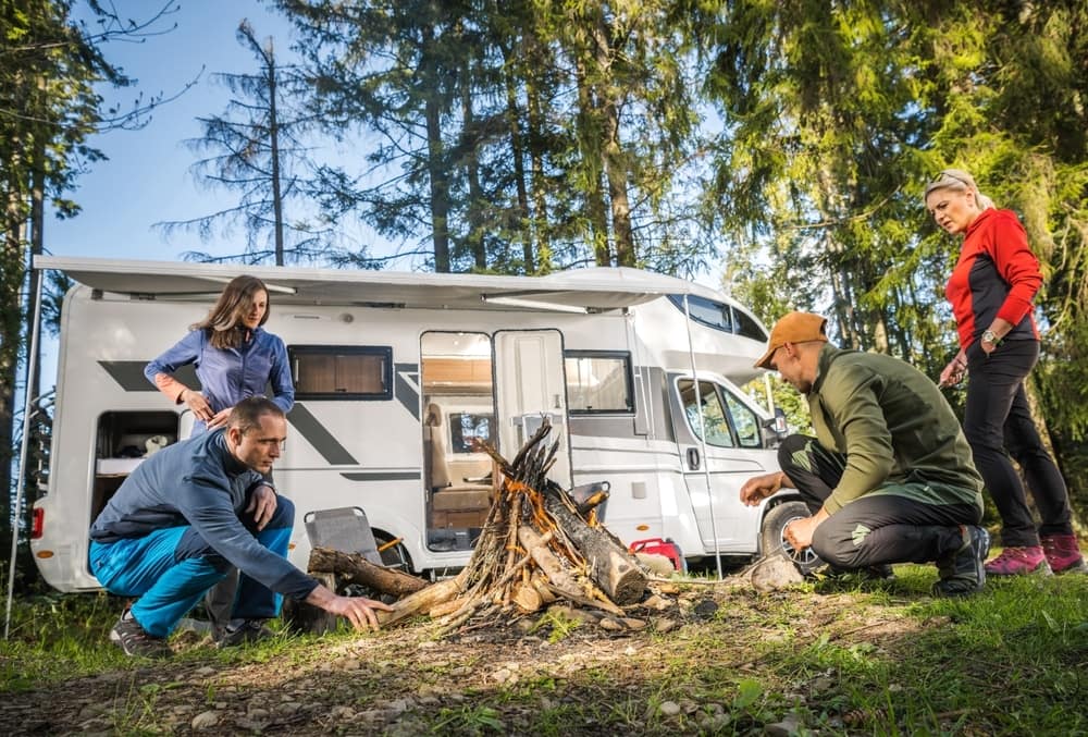 A group of people standing around a campfire near an RV.