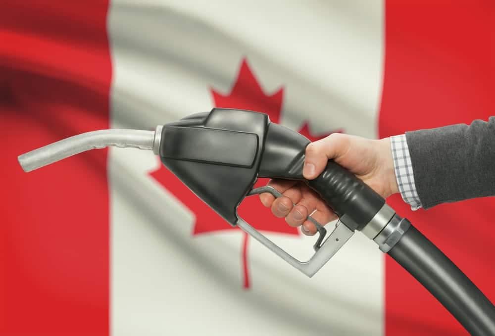 A man is holding a gas pump in front of a Canadian flag, showcasing the innovative advancements in the fuel industry.