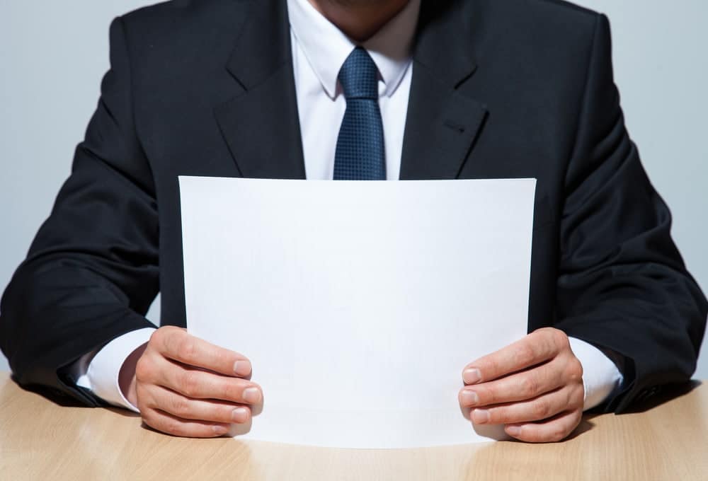 A man in a suit holding a proposed blank sheet of paper.