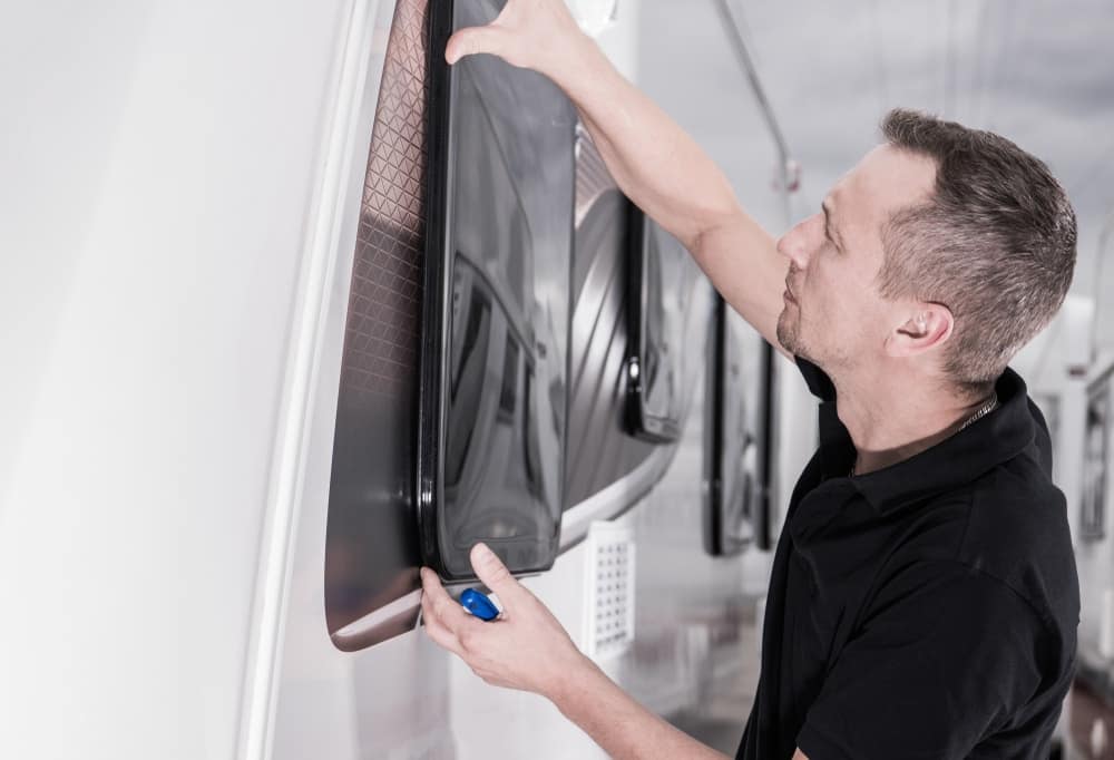 A man repairing a window on an RV, adhering to Emission Standards set by the EPA.