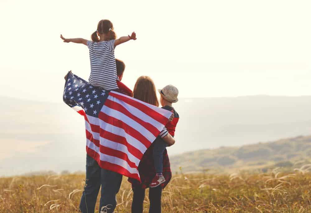 An outdoor recreational family proudly holding an American flag in a field.