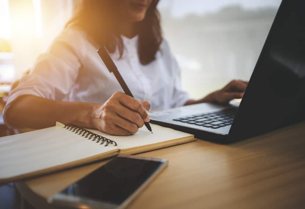 A woman utilizing Roadpass Digital resources while writing on a notebook at a desk.