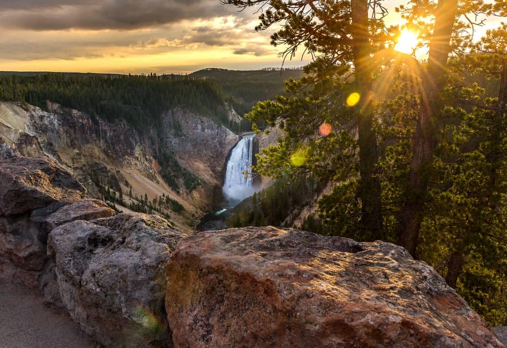 The sun is setting over a waterfall in Yellowstone National Park, highlighting the natural beauty of this iconic location.