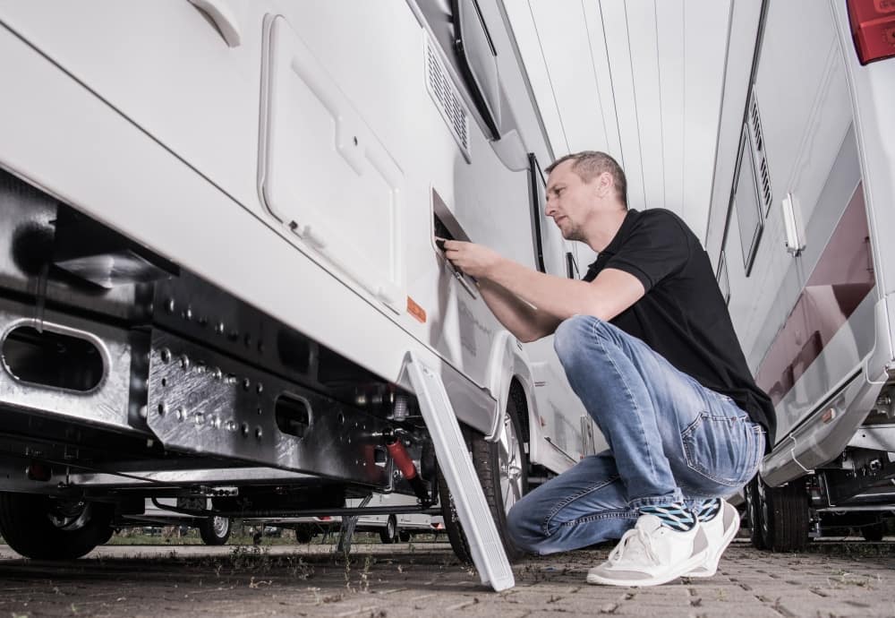An RV technician working on an RV in a parking lot.