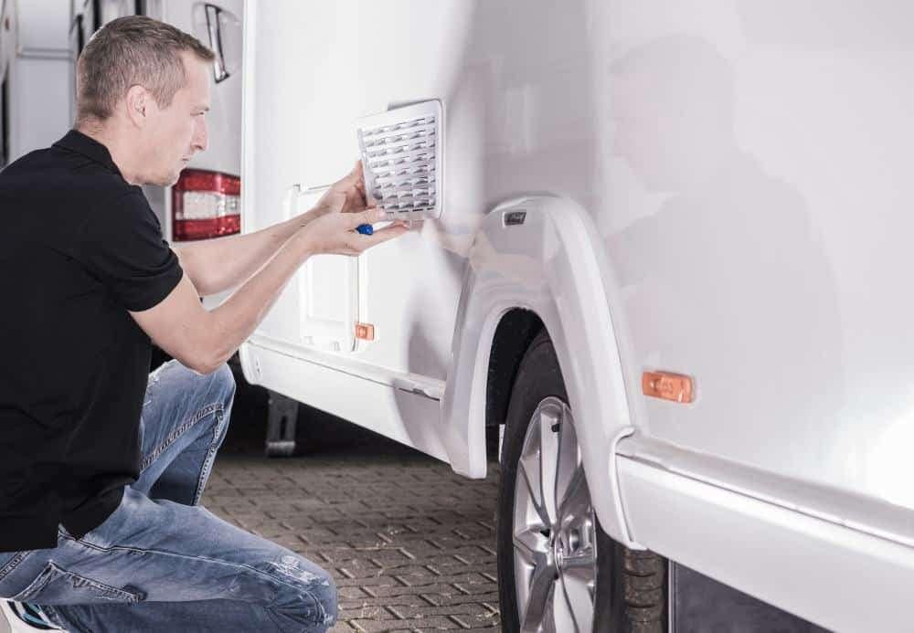 A certified technician performing fixed operations on an RV, specifically fixing a lock on a white vehicle.