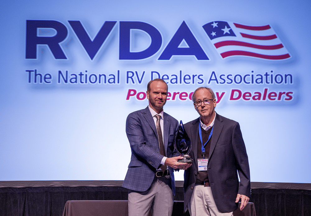 Two men standing in front of a sign at the RV Dealers Convention.