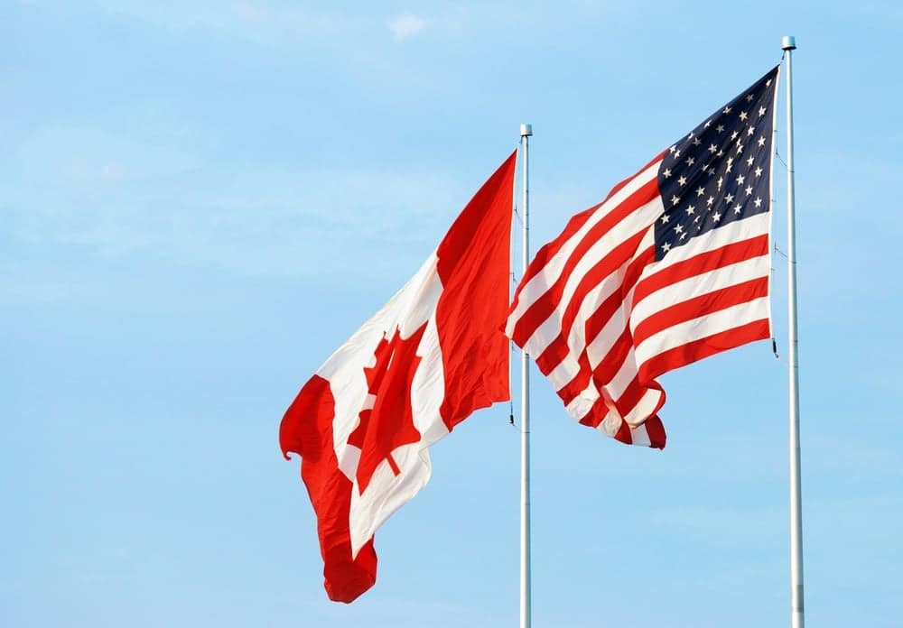 Two Canadian and American flags proudly flying in the wind to symbolize Canada-U.S. tourism.