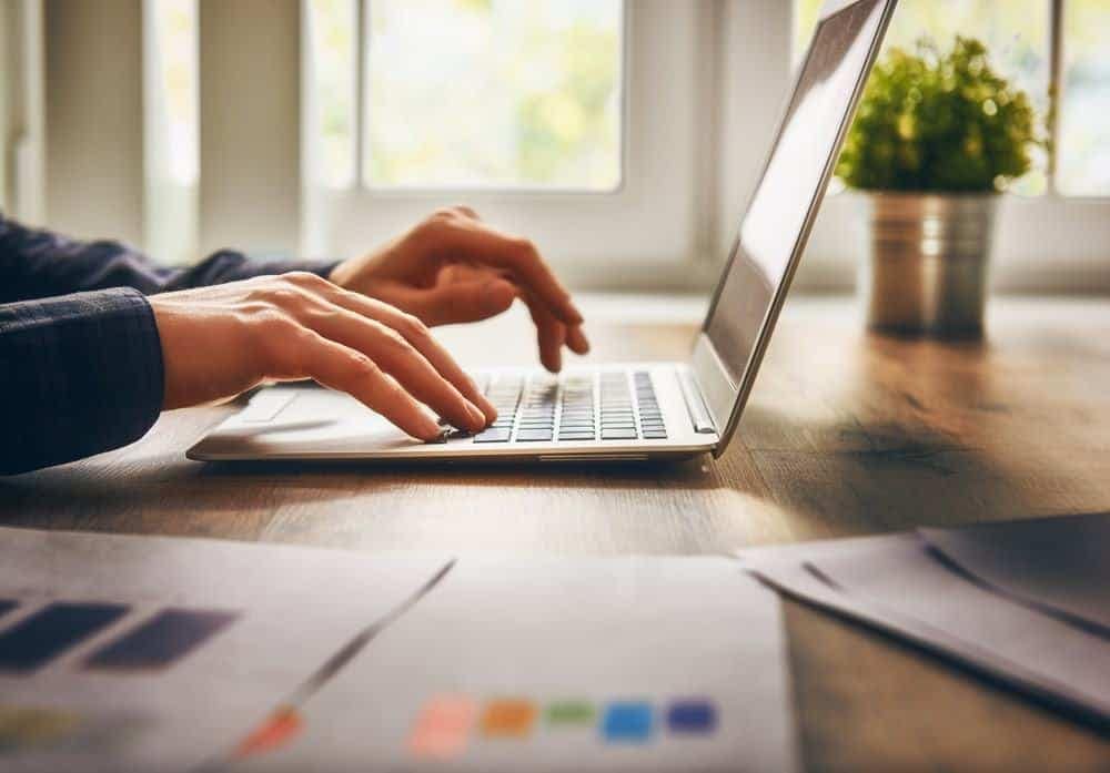 A person typing on a laptop at a desk while working on a website project.