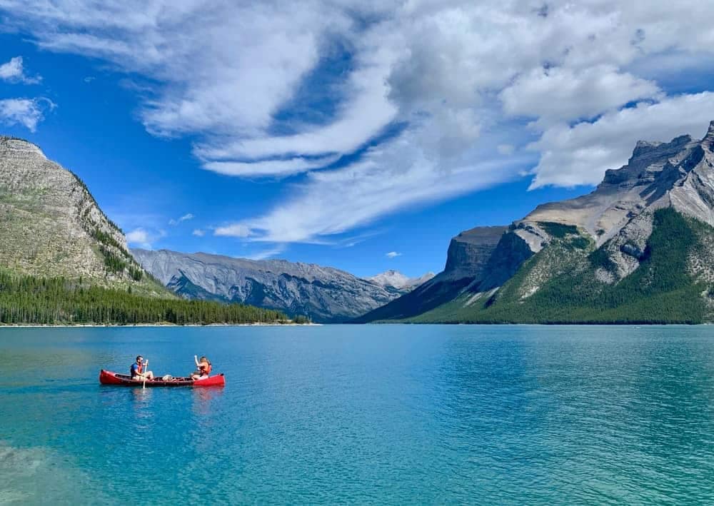 Visitors in Banff National Park enjoy paddling in a canoe on a serene lake, with breathtaking mountains forming a majestic backdrop.