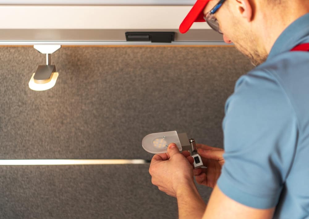 A Mobile RV Technician in a red hat is working on a light fixture.