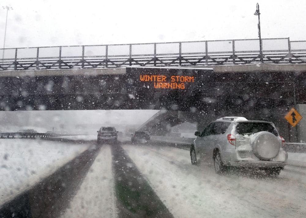 A car driving on a highway with a sign that says winter storm warning.