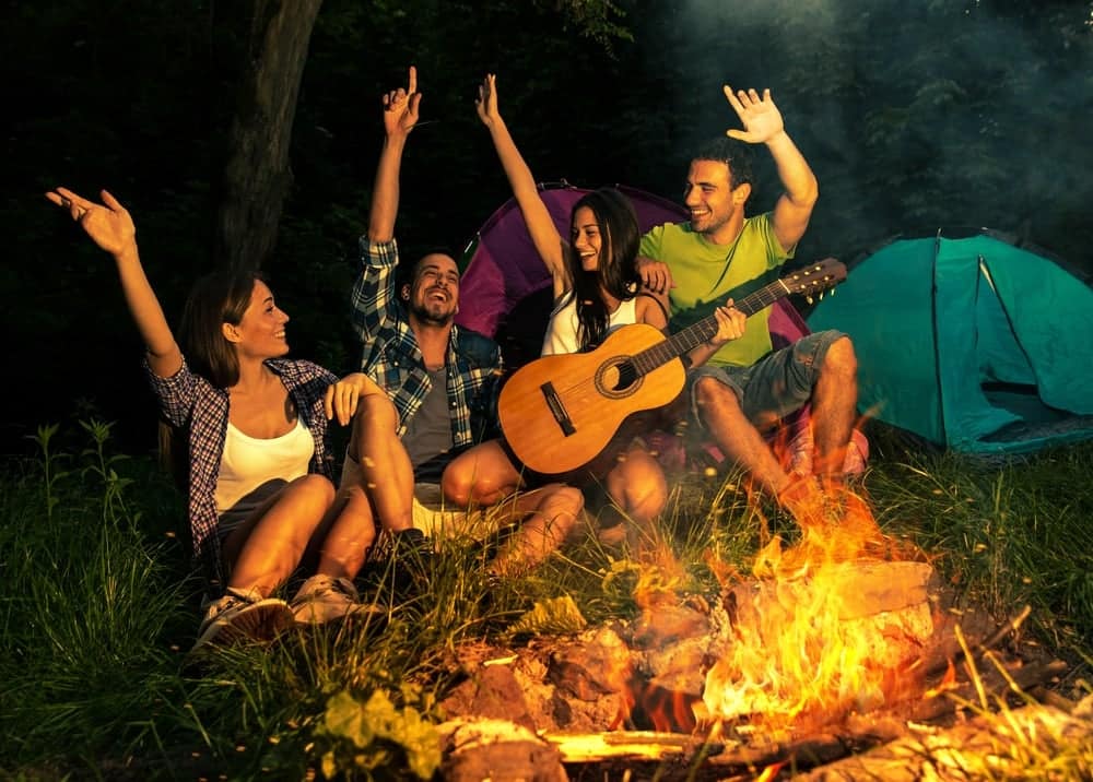 A group of friends sitting around a campfire, playing music with guitars in Michigan.