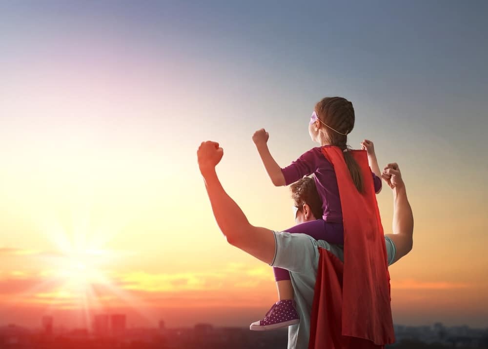 Father and daughter in superhero capes at sunset, celebrating Father's Day activities.