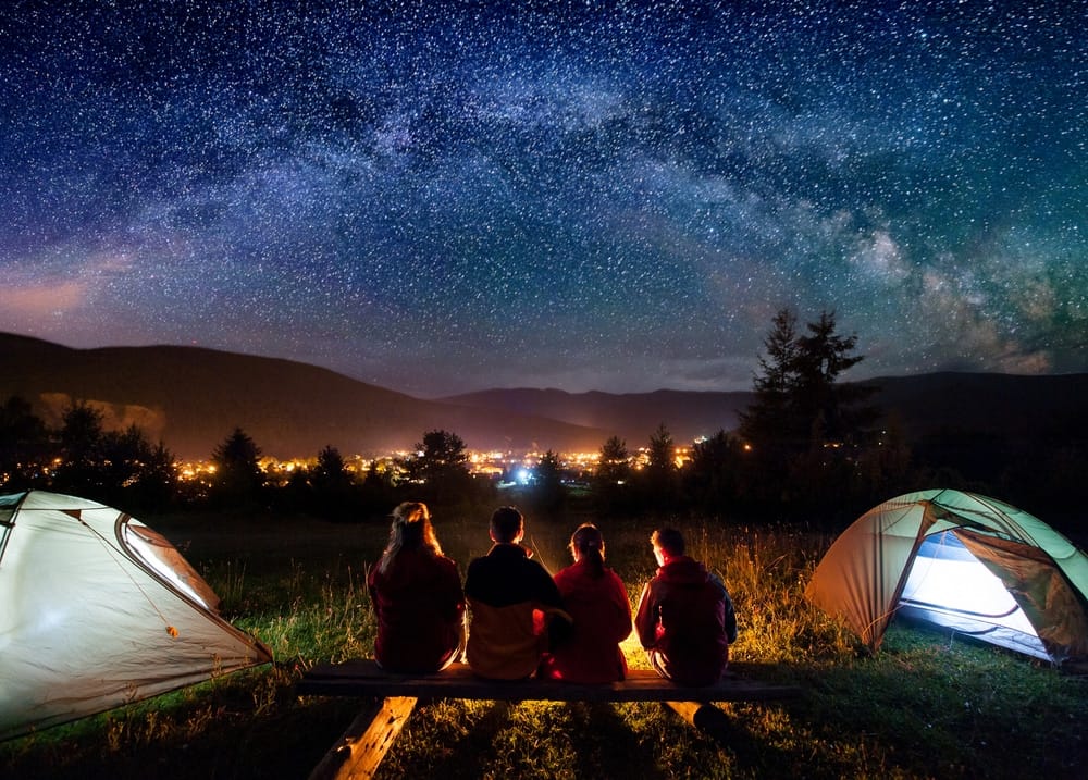 Last-Minute camping on July Long Weekend, a group of people sitting around a campfire under a starry sky.