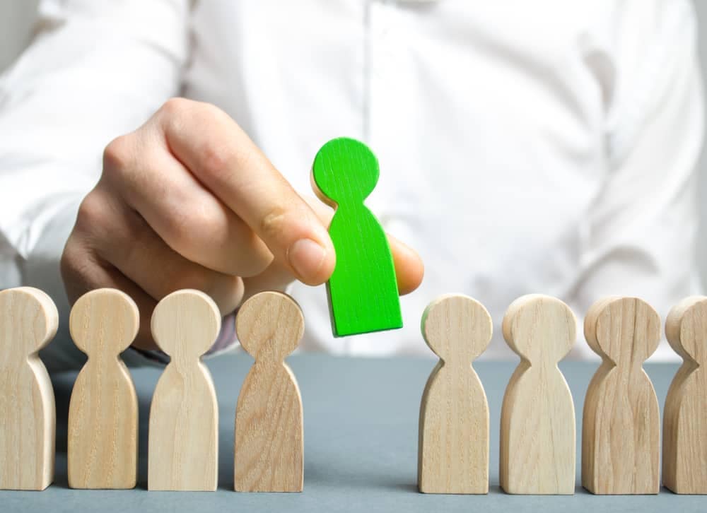 A man, Eric Rathburn, is placing a green figure in front of a group of wooden people.