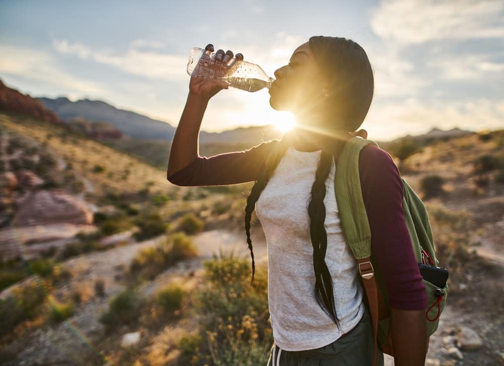A woman drinking water from a bottle in the desert, promoting Climate Action.