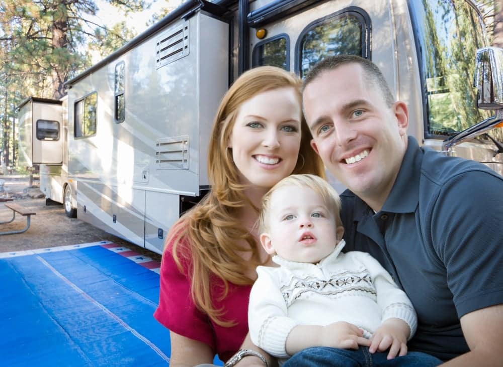A family with a baby enjoying their time in front of an RV at FamCamp.