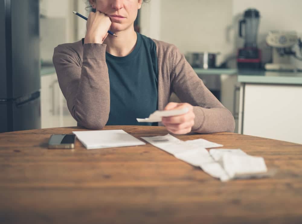 A less confident woman is sitting at a table with papers and a cell phone.