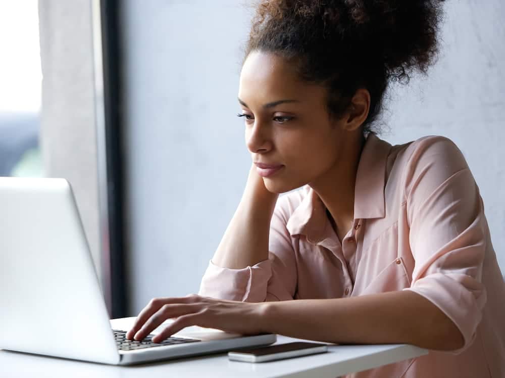 A woman sitting at a table looking at her laptop, analyzing RoverPass Owner Reports.