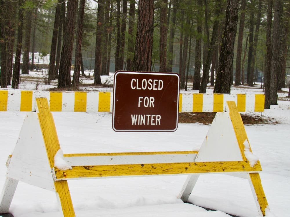 A yellow and white sign that says closed for winter near a nearby campground.
