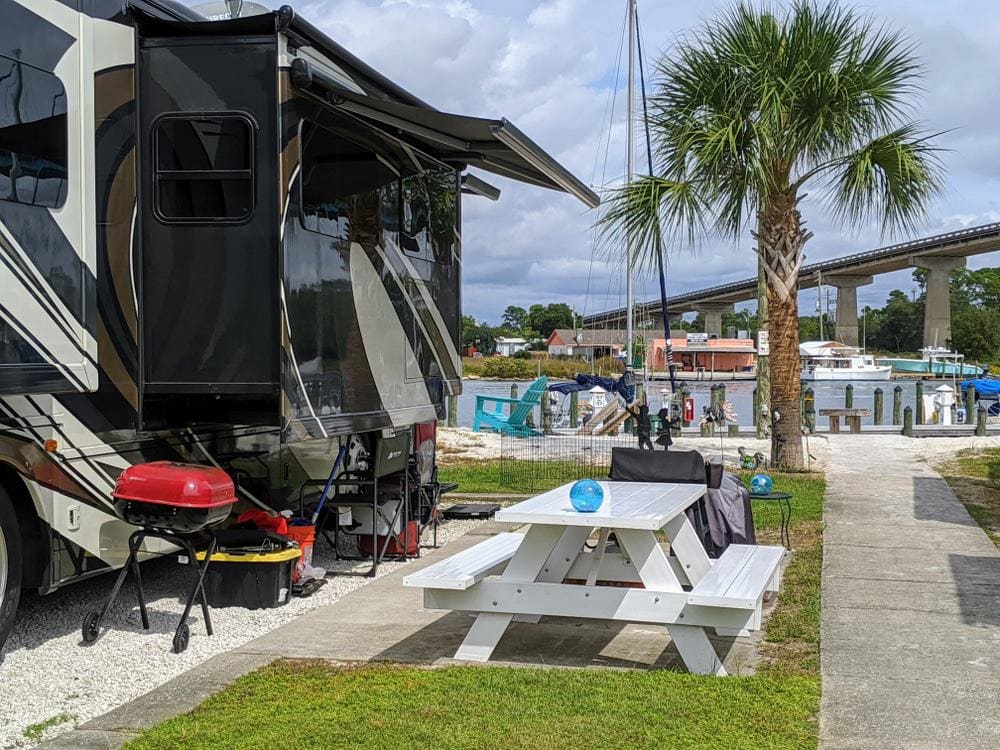An Approved RV Park in North Carolina with a rv parked next to a picnic table and palm trees.