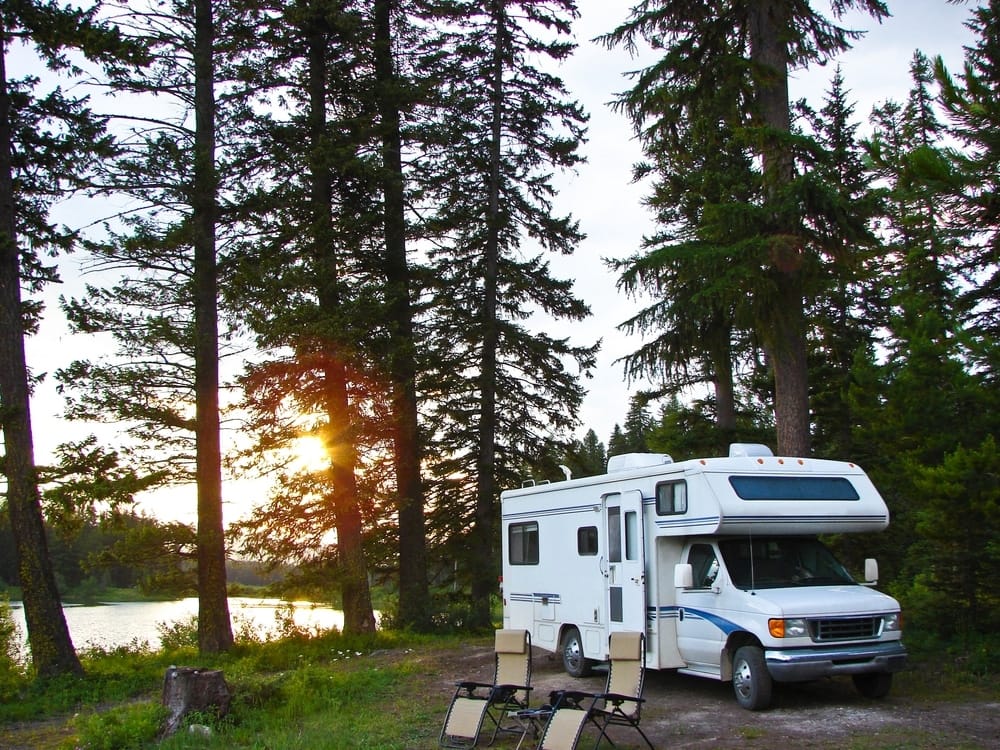 A white RV parked next to a serene lake in the enchanting woods.