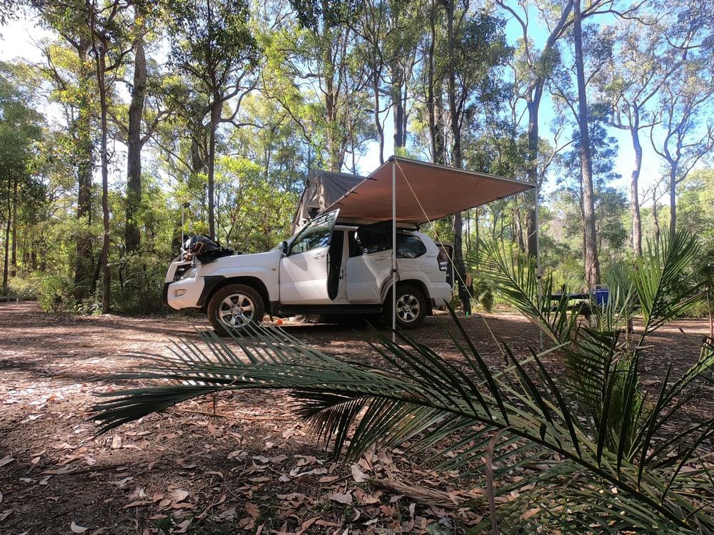 A jeep parked in the woods at a campground, with an awning.
