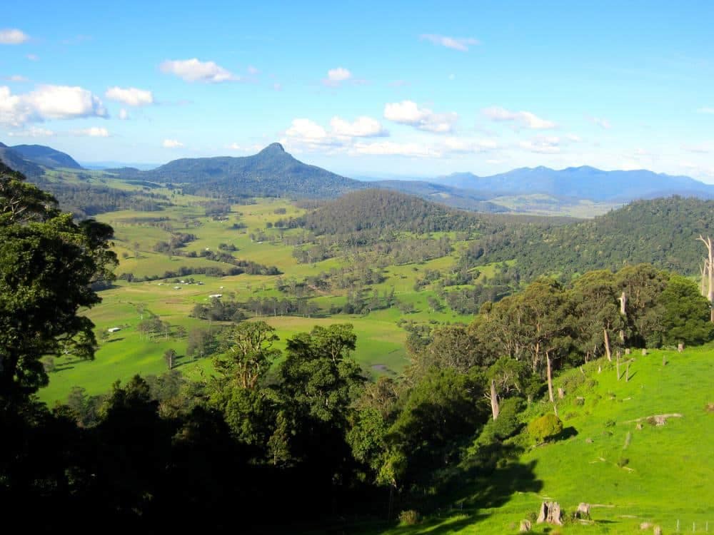 A view of a lush green valley with mountains in the background. The breathtaking scenery is reminiscent of the stunning landscapes found in Australia, particularly at Spring Creek Caravan Park. The park's recent