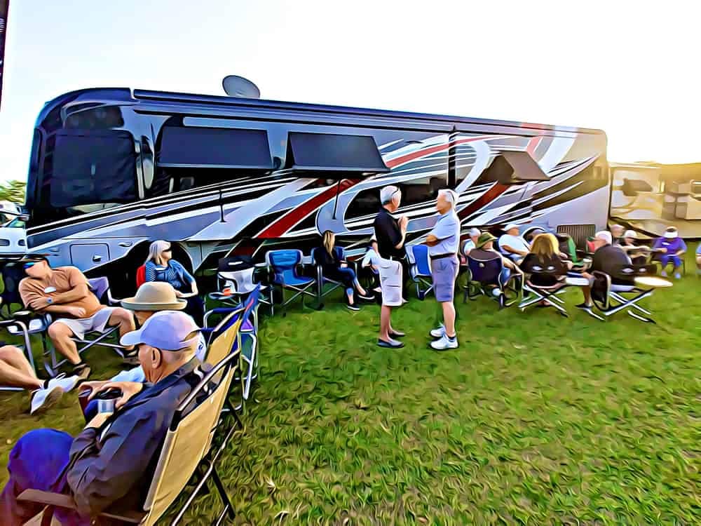 A group of people sitting in lawn chairs near an RV at an FMCA Rally.