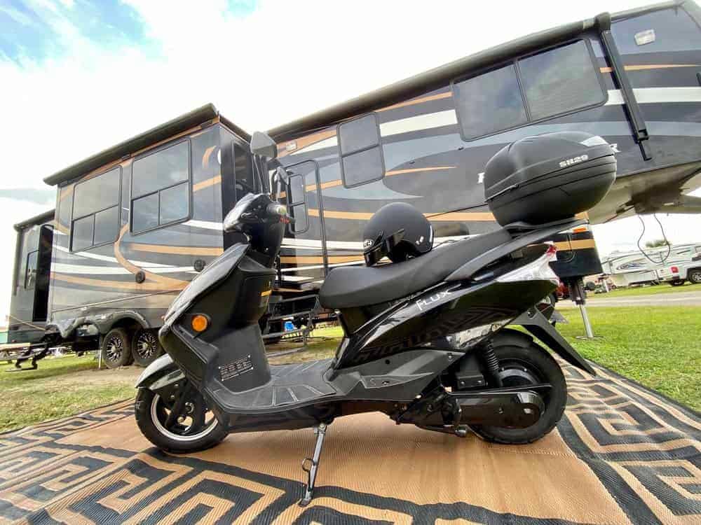 A Flux Mopeds scooter is parked in front of an RV at a campground.