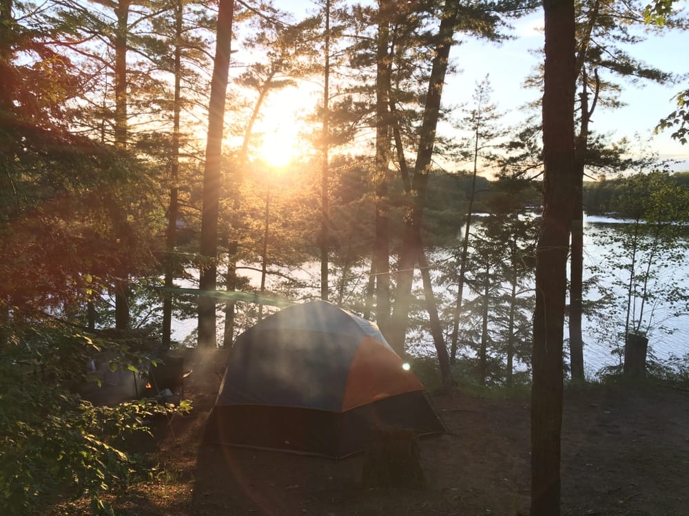 The sun is setting behind a tent in the woods, providing a captivating visitor experience.