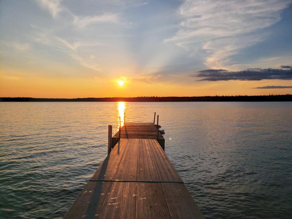 A dock on a lake in Duck Mountain Provincial Park with the sun setting behind it, offering an idyllic spot for outdoor recreation in two provinces.