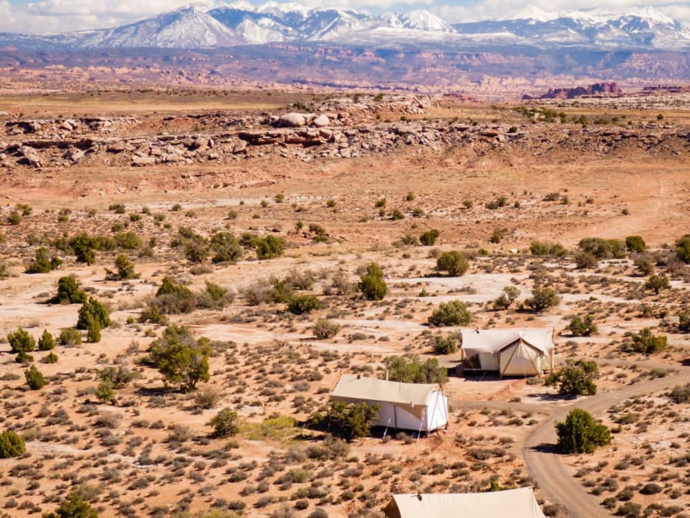 An aerial view of a small cabin in the Utah desert with mountains in the background, located at Under Canvas Resort.