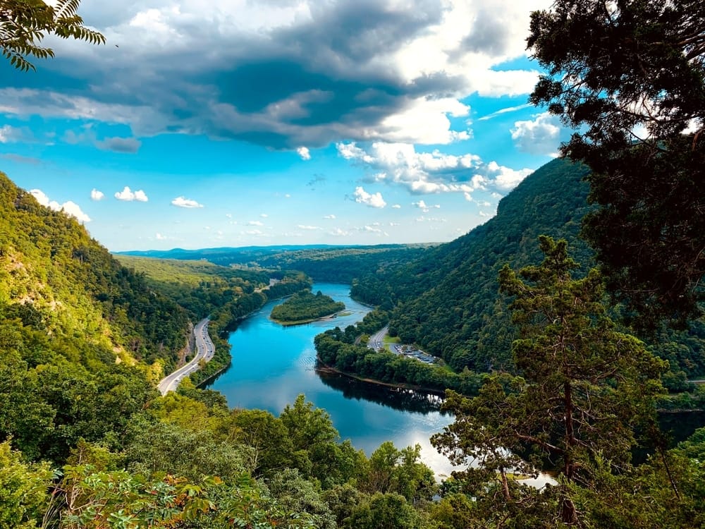 A breathtaking view of a river enveloped by dense trees and towering mountains.