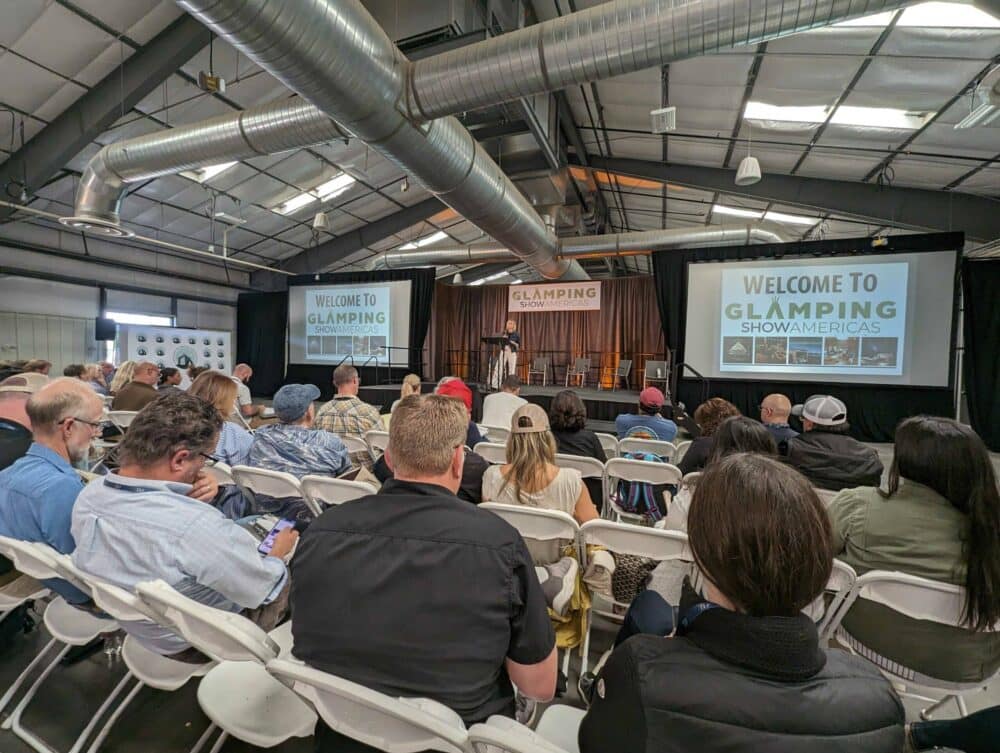 The 2023 Glamping Show Americas begins as a group of people sitting in chairs in a large room.