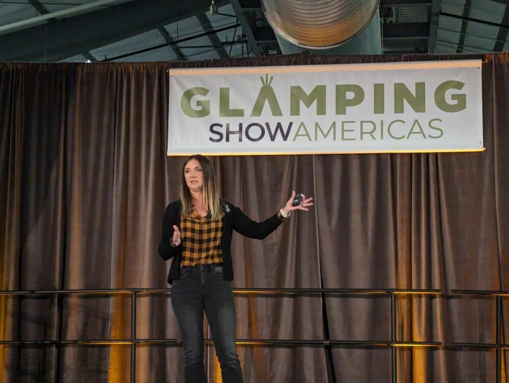 A woman standing in front of a sign that says glamping show americas, showcasing the hospitality of the glamping industry.