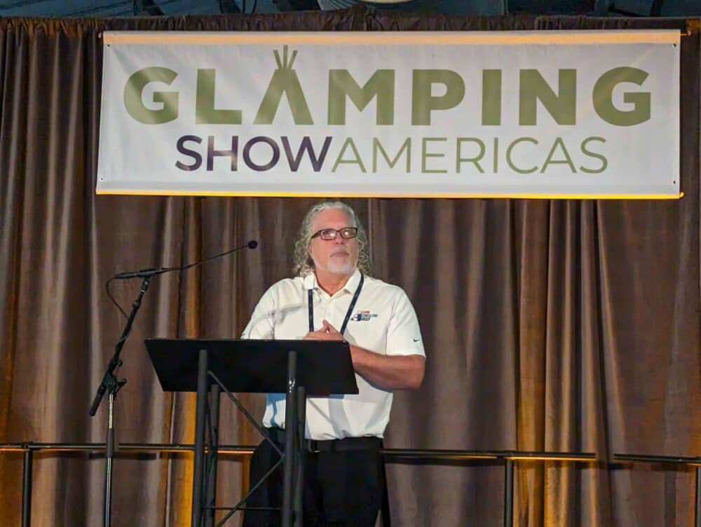 A man standing at a podium presenting the industry report on the rapid growth of glamping in America at the Glamping Show Americas.