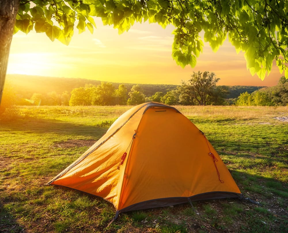 Campers set up a tent in a picturesque New England field at sunset, providing insights into the beauty of outdoor adventures.