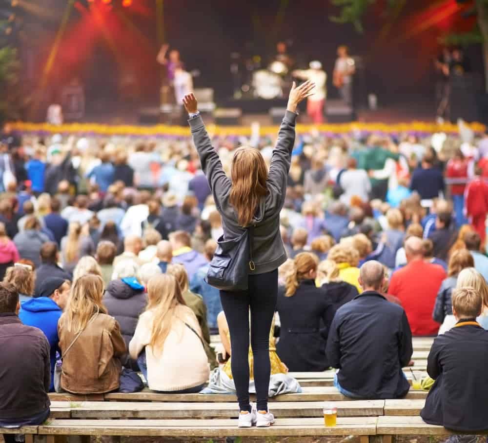 A woman raising her arms in the crowd at a music festival in Auburn, surrounded by RV and Camping enthusiasts.