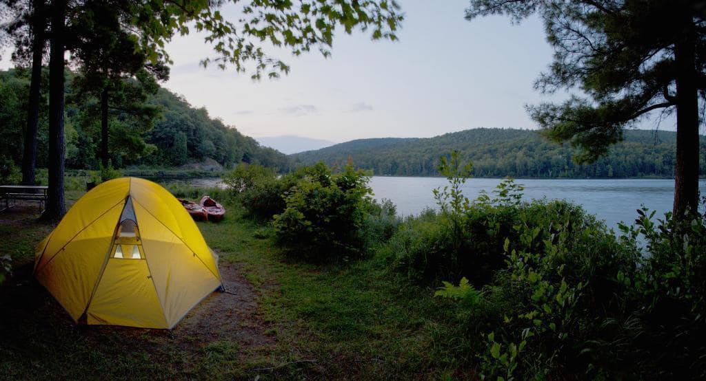 An Auto Draft lit tent near a tranquil lake at twilight with kayaks nearby.
