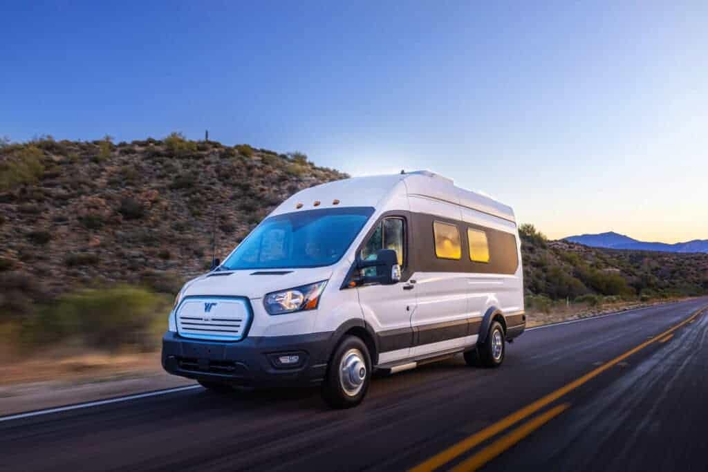 The 2019 Ford Transit RV, manufactured by Winnebago, is driving down a desert road.