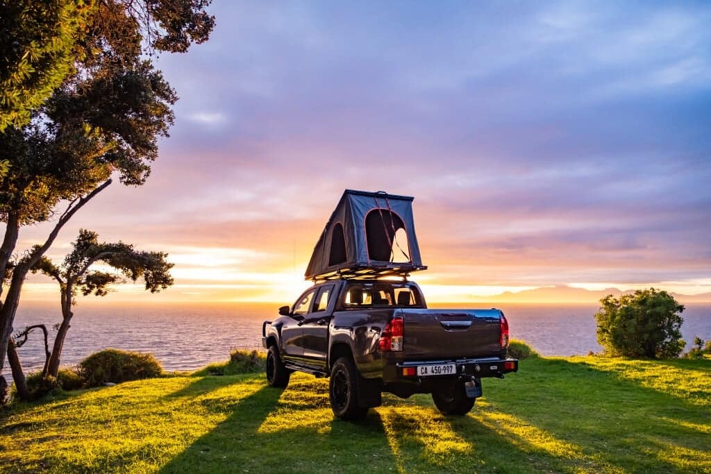 A lightweight truck with a tent on top of it near the ocean.