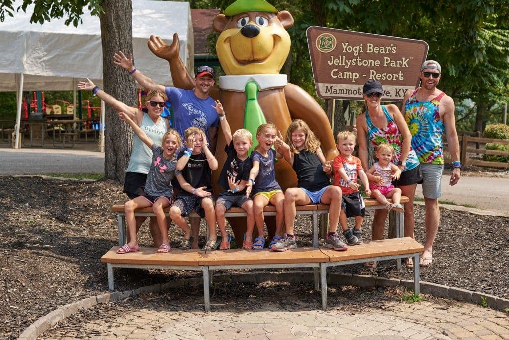 A Yogi Bear-themed group posing in front of a bear statue at one of the Jellystone Park locations nationwide.