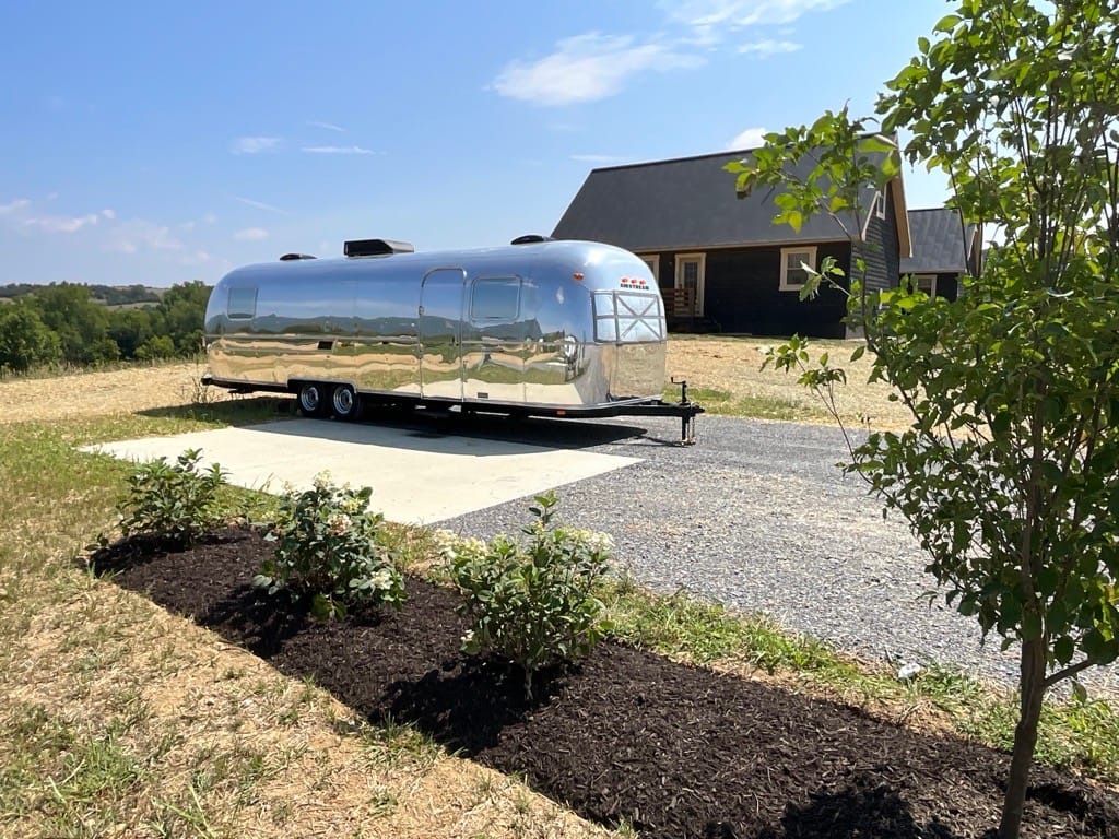 A silver airstream trailer parked in front of a house at the Luray RV Resort.