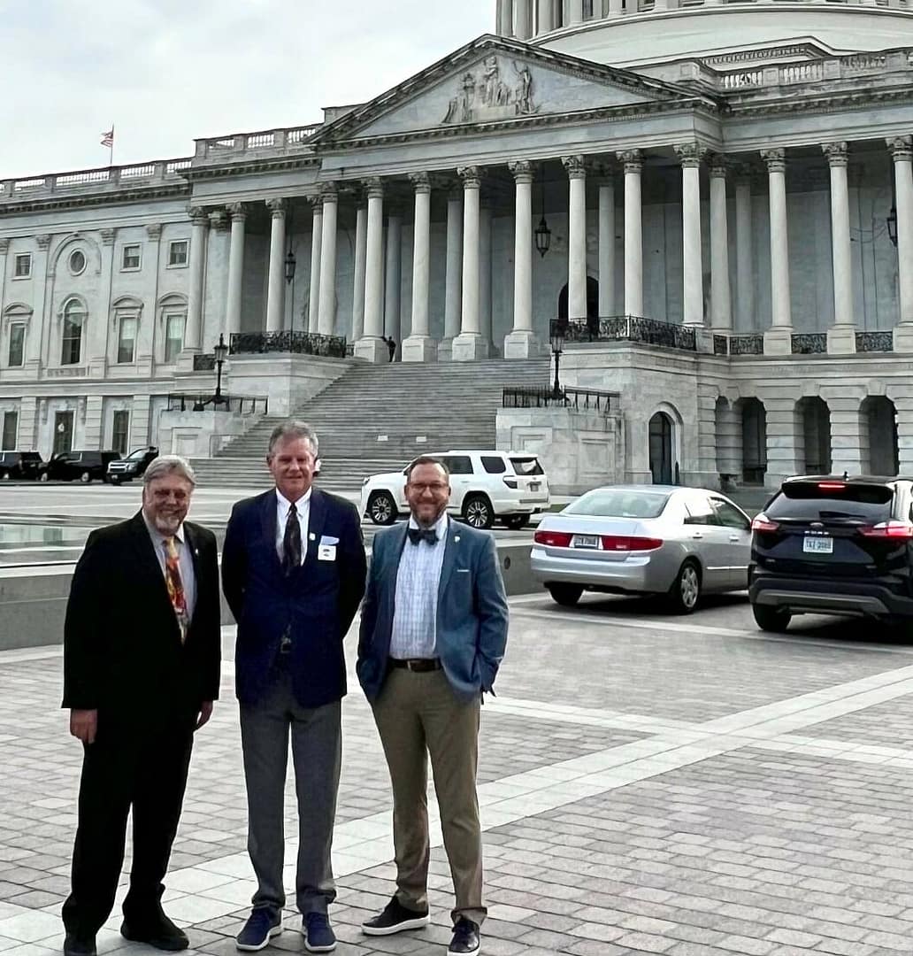 Three men standing in front of the United States Capitol building on a cloudy day.